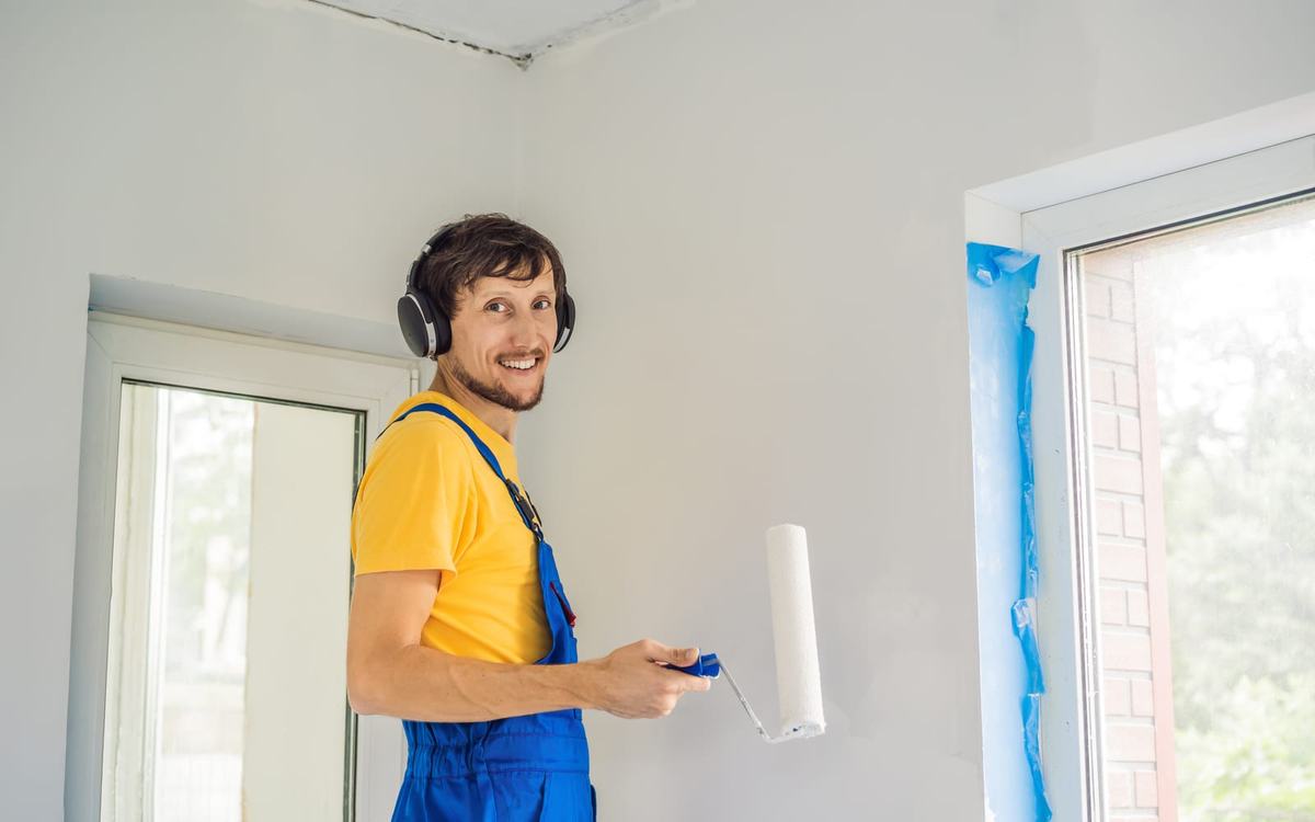 Painter rolling a fresh coat onto an interior wall in a bright, empty room