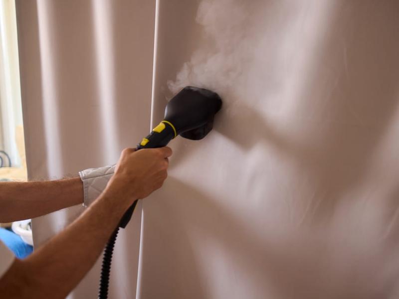 Softening and lifting old wallpaper from a wall with a stripping tool