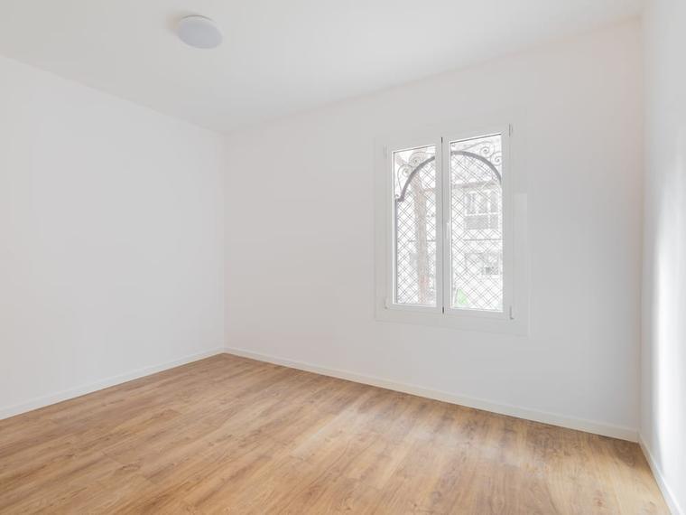 Empty apartment room with newly painted white walls, laminate flooring and a bright window