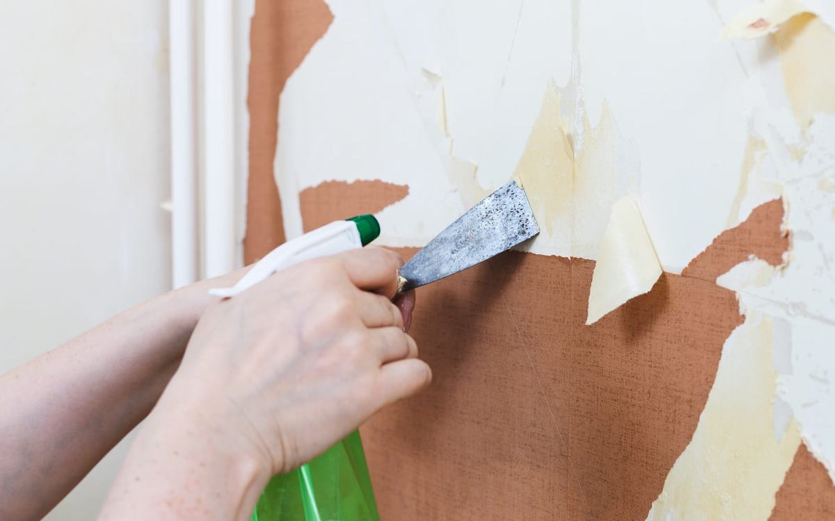 Old wallpaper being stripped away from a wall during a room renovation